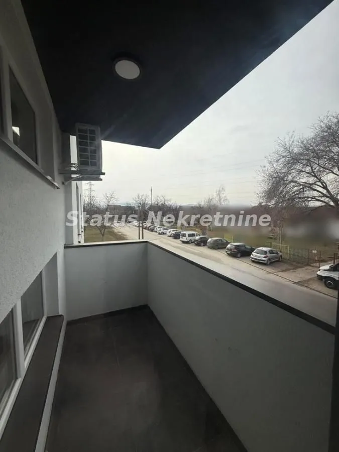 Natkriveni balkon sa pogledom na ulicu i parkirana vozila.