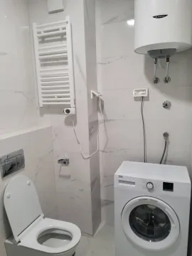 Small bathroom with white tiles, toilet, and washing machine. - image 8