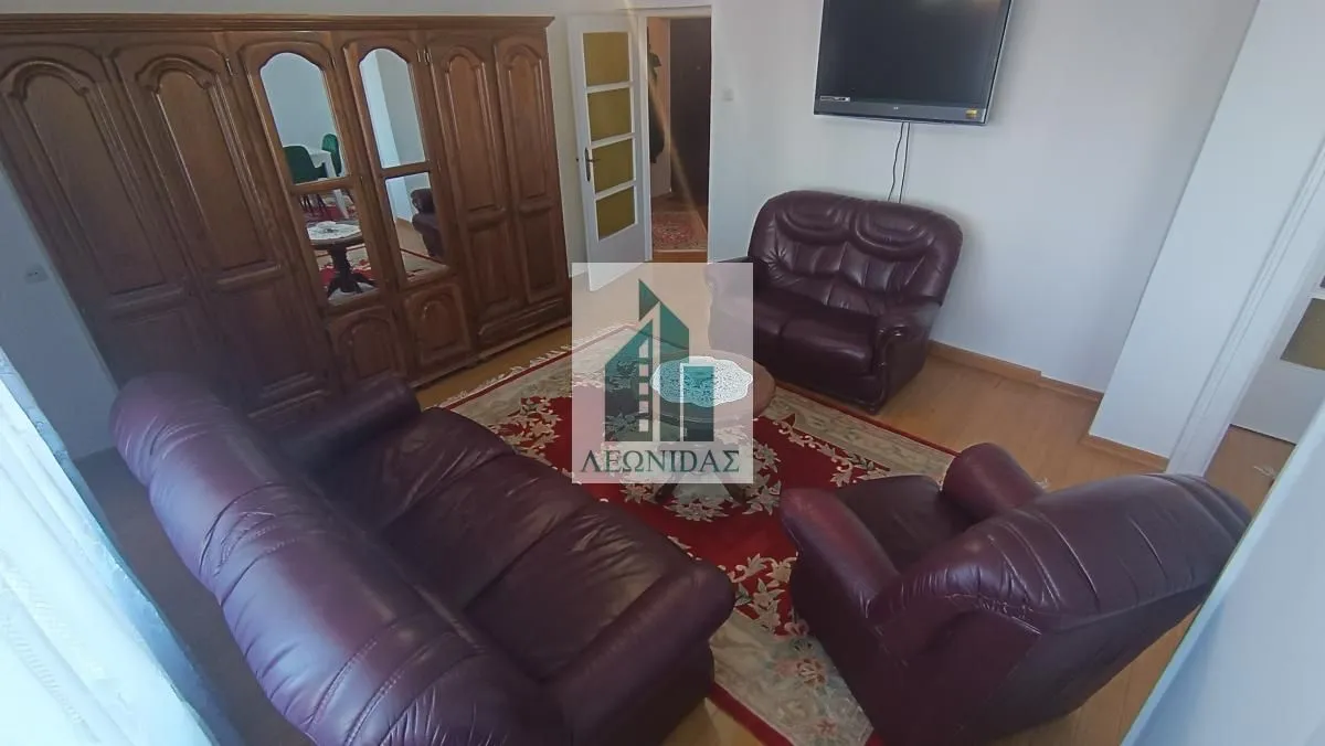 Living room furnished with a seating set, a large wardrobe, and a wall-mounted TV.