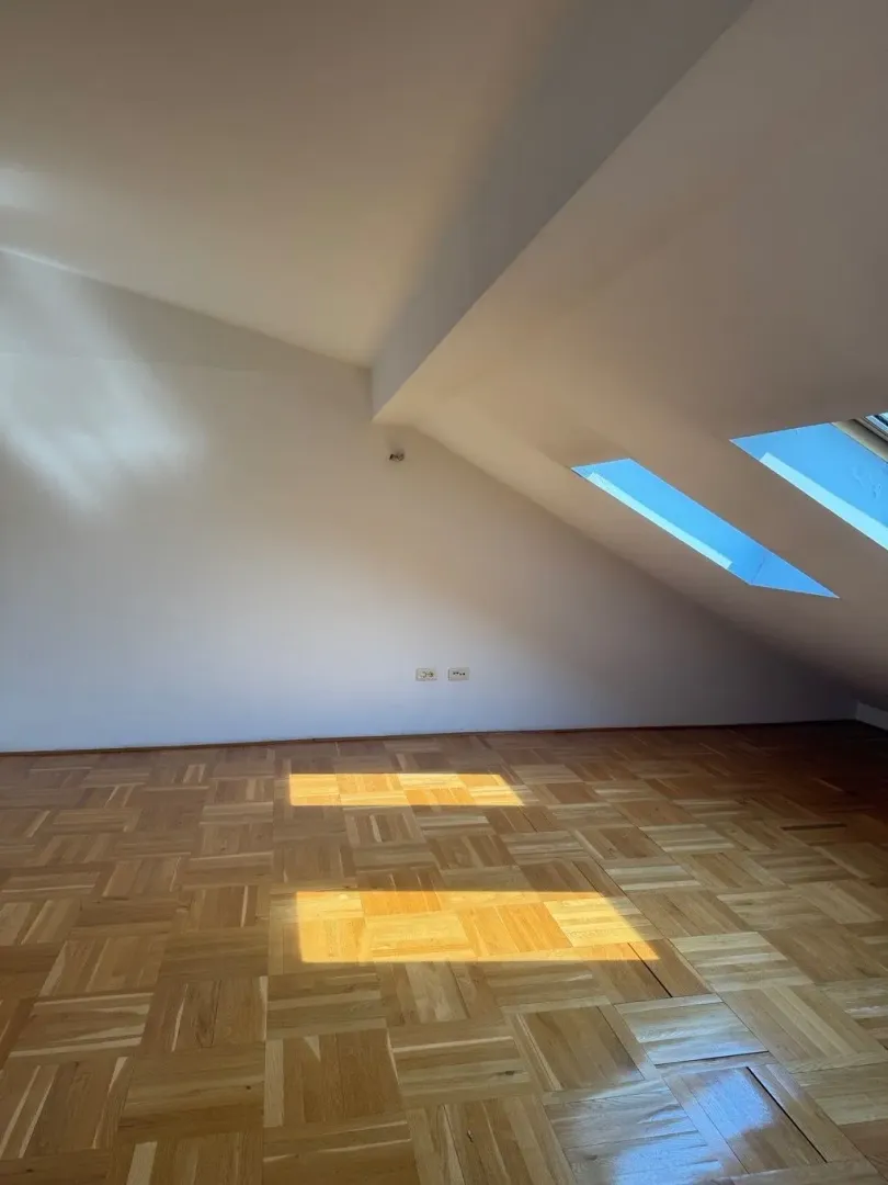 Empty attic room with parquet flooring and skylights.