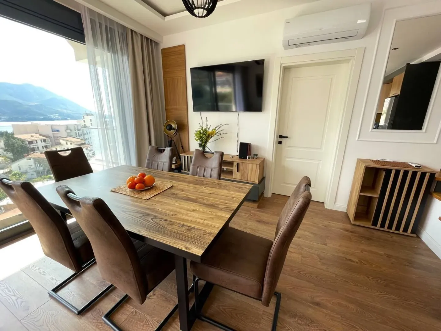 Living room with a dining table and chairs, wall-mounted TV, and a sea view.