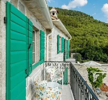 View of the spacious balcony of a traditional stone house with green shutters.