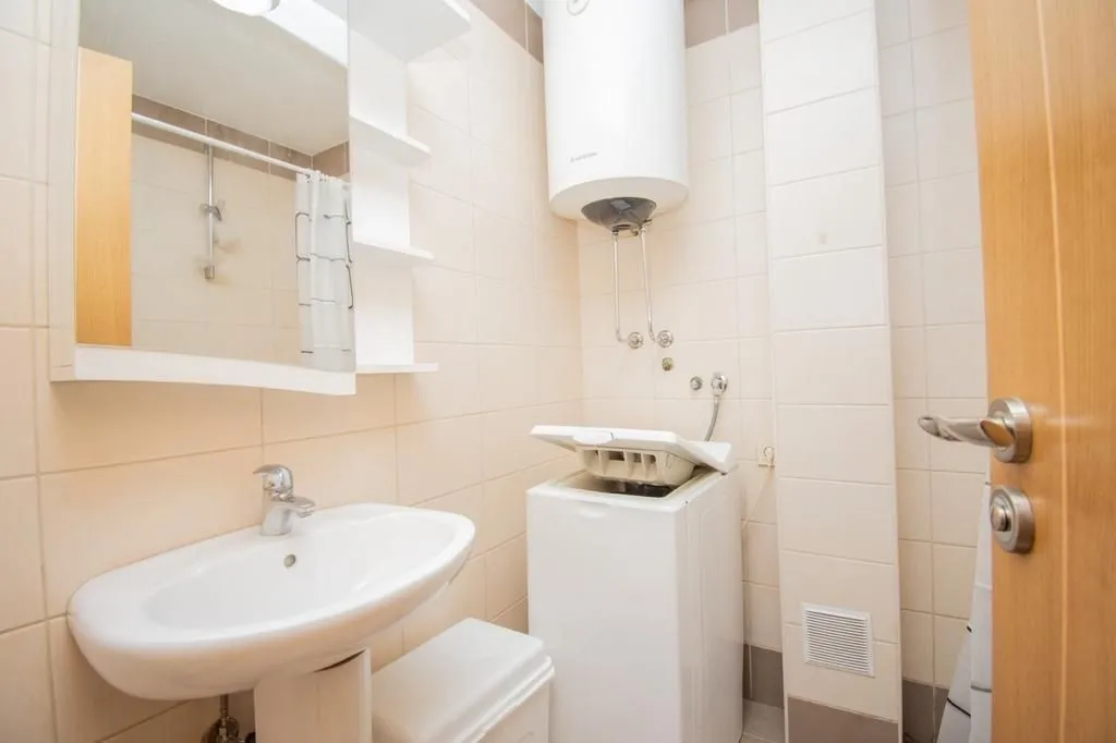 Bright bathroom with a sink, mirror, and washing machine.