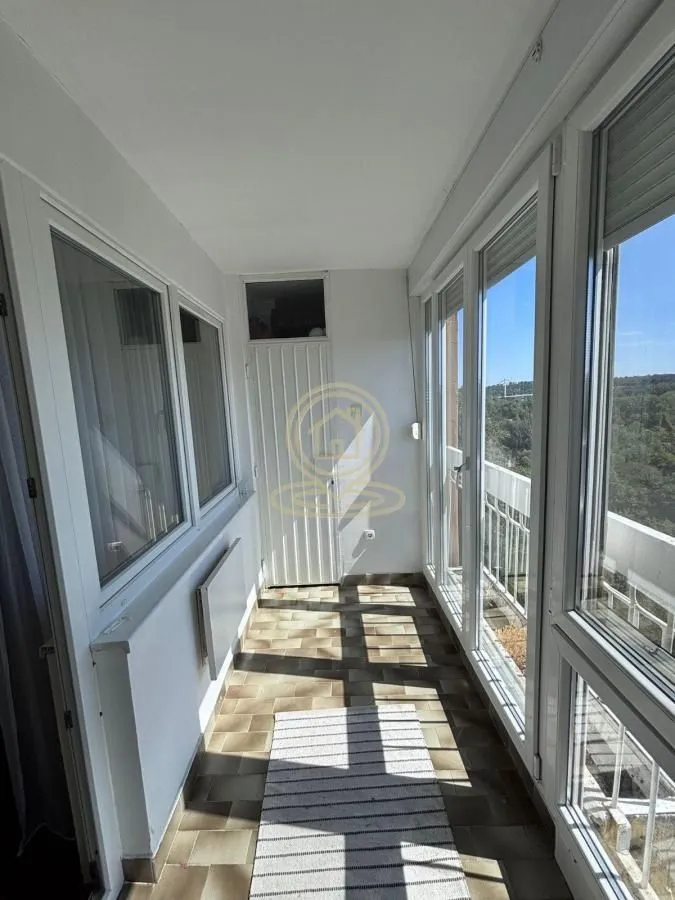 Zastakljeni balkon sa keramičkim pločicama na podu i pogledom na prirodu.