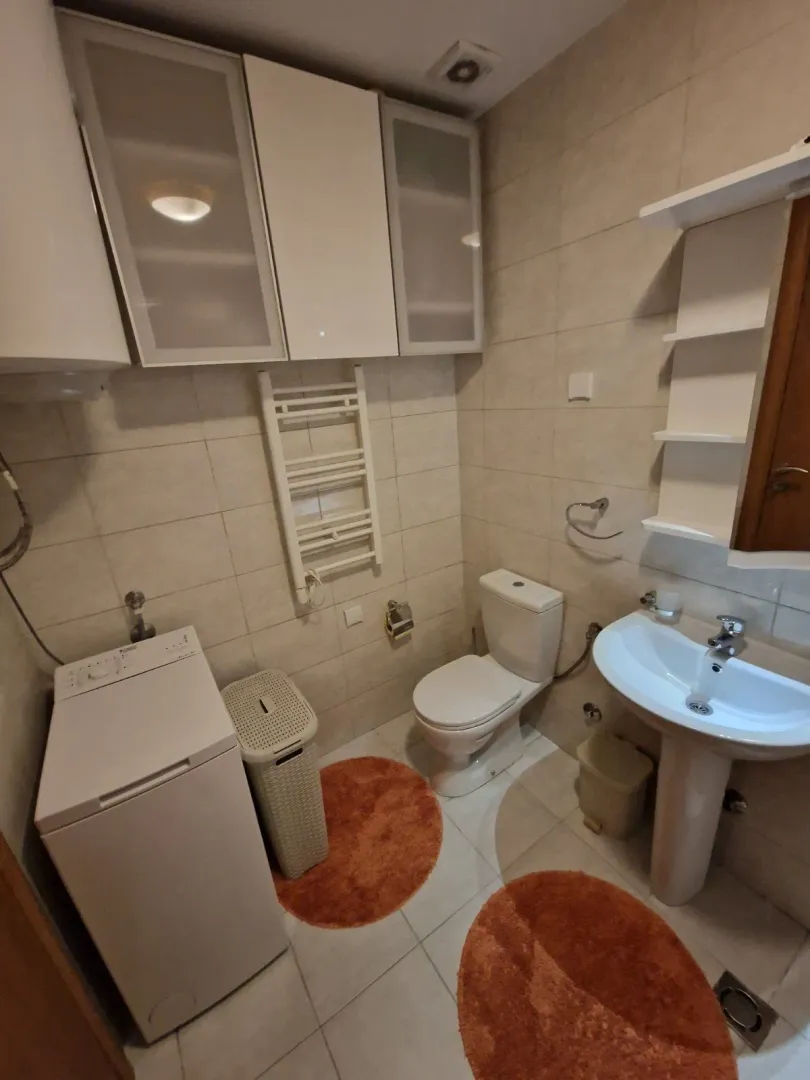 Manje kupatilo sa umivaonikom, WC šoljom, veš mašinom i zidnim elementima.
