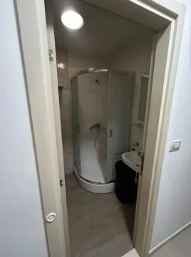 Pogled kroz vrata na manje kupatilo sa tuš kabinom i umivaonikom. - image 9