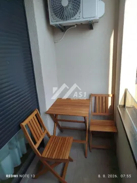 Manji balkon sa drvenim stolom i dve stolice i klima uređajem na zidu. - image 2