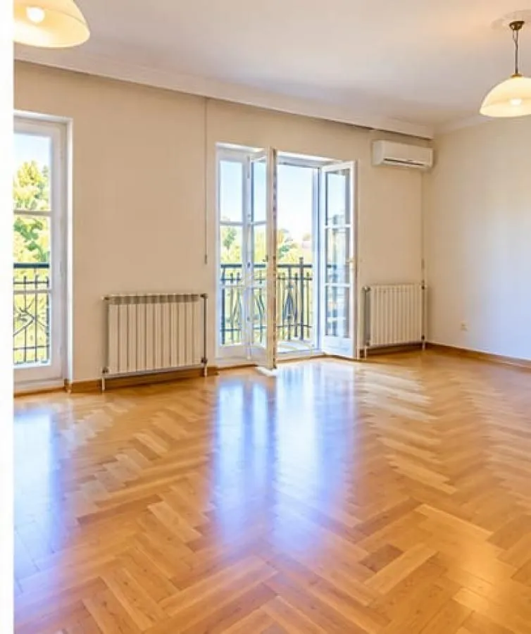 Spacious empty room with parquet flooring and access to a balcony.