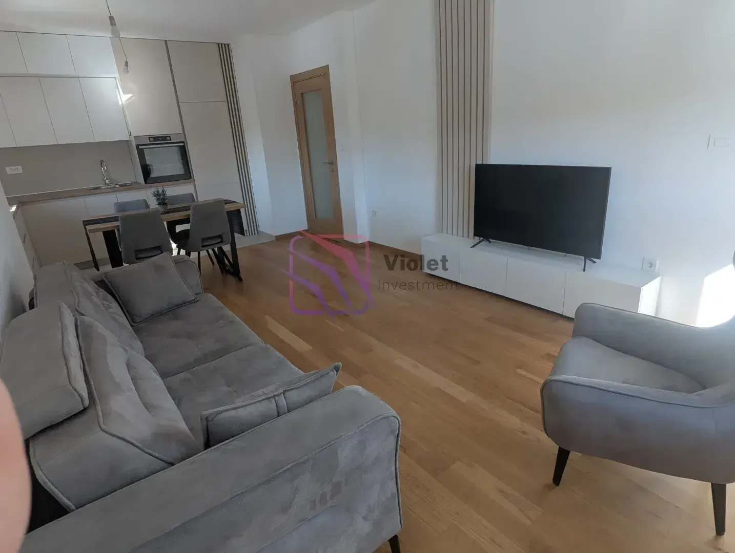 Living room with a sofa, TV, and dining area in the background.