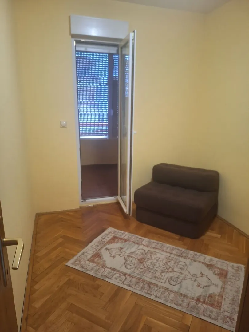 Manja soba sa parketom, foteljom na razvlačenje i izlazom na terasu.
