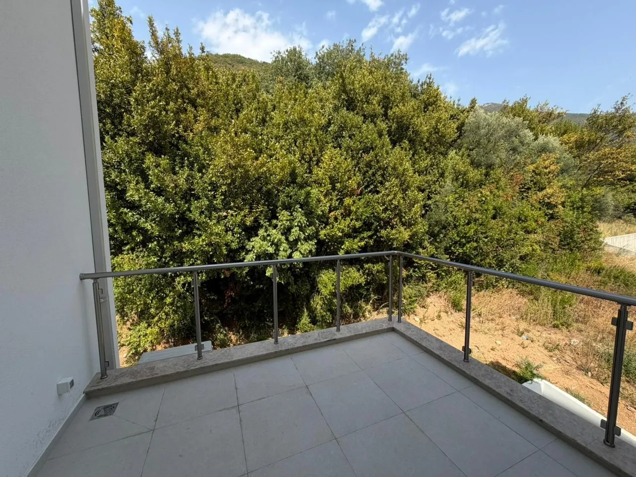 Manji popločani balkon sa metalnom ogradom i pogledom na zelenilo.
