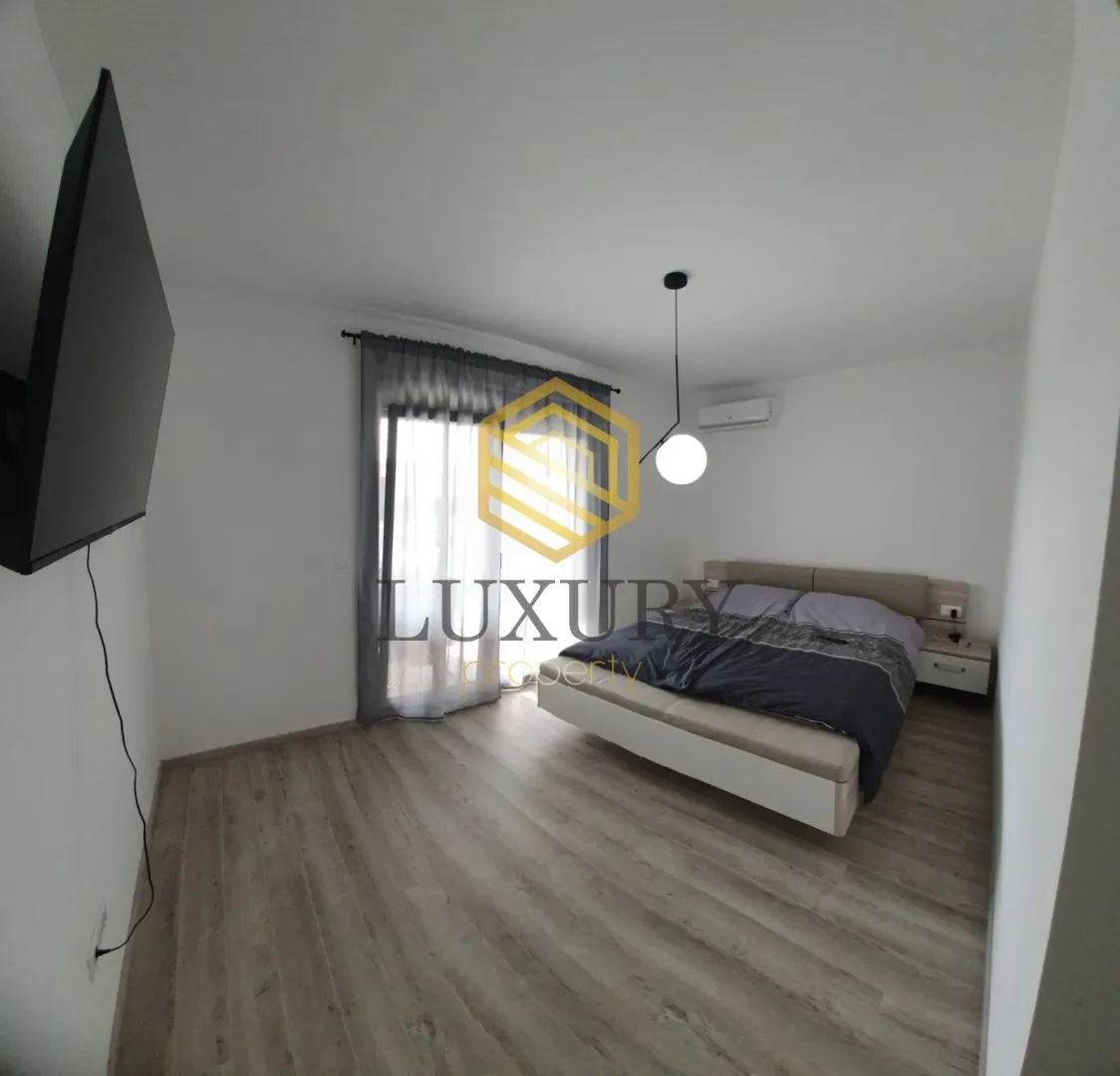 Modern bedroom with a double bed, wall-mounted TV, and access to the terrace.