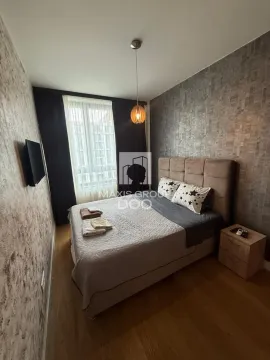 Nameštena spavaća soba sa bračnim krevetom, noćnim stočićem i televizorom na zidu. - image 7