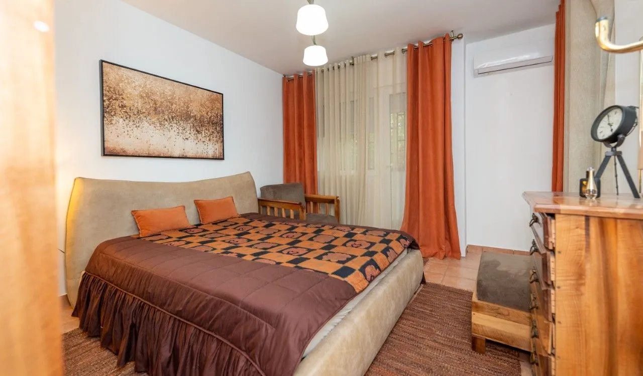 Furnished bedroom with a double bed, dresser, and orange curtains.