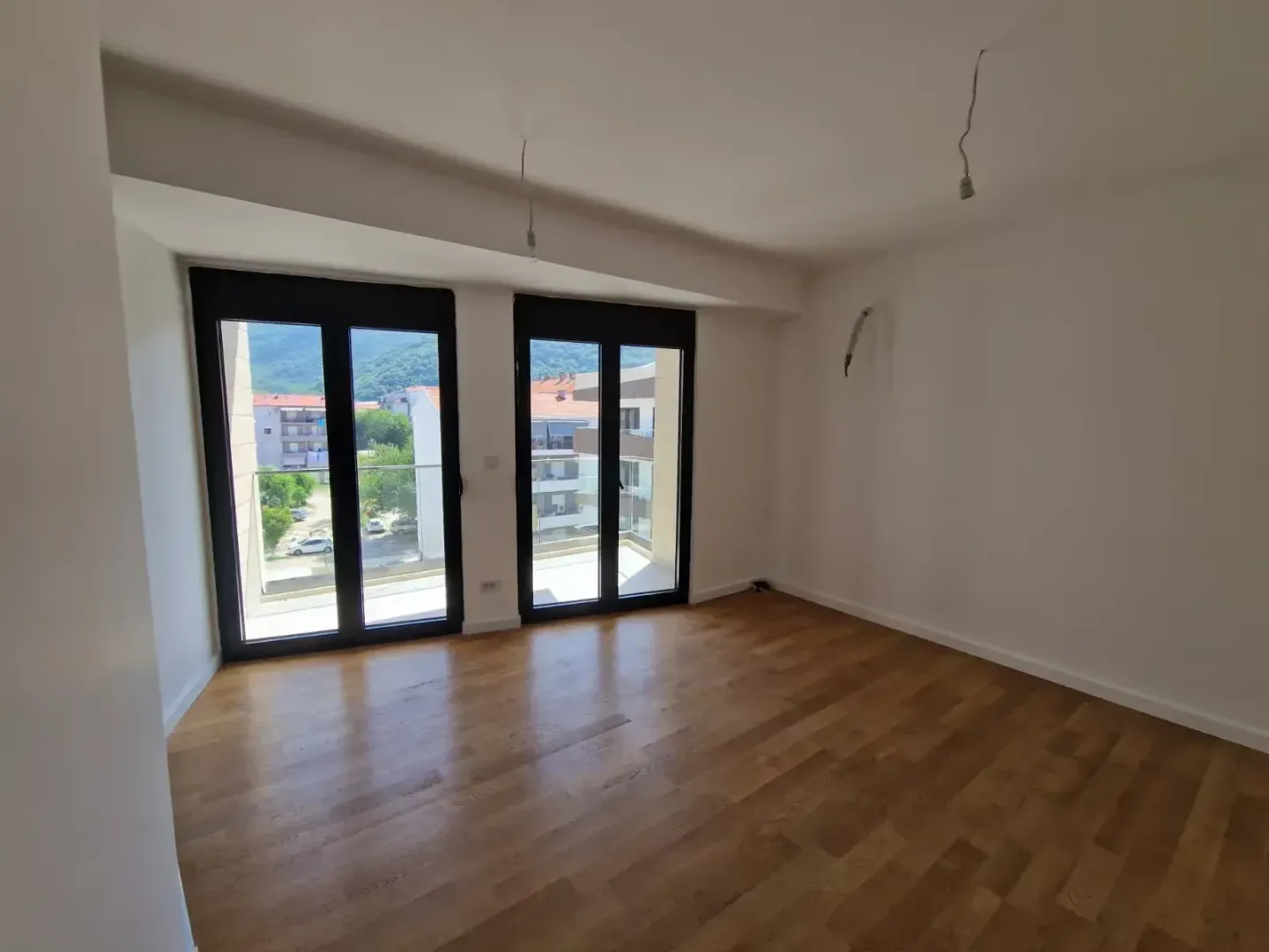 Prazna soba sa parketom i dvokrilnim staklenim vratima koja vode na balkon.