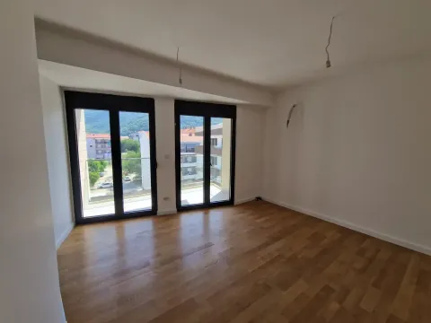 Prazna soba sa parketom i dvokrilnim staklenim vratima koja vode na balkon. - image 7