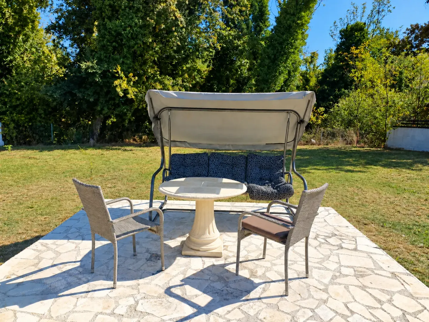 Yard with a stone-paved terrace, garden table, chairs, and a swing.