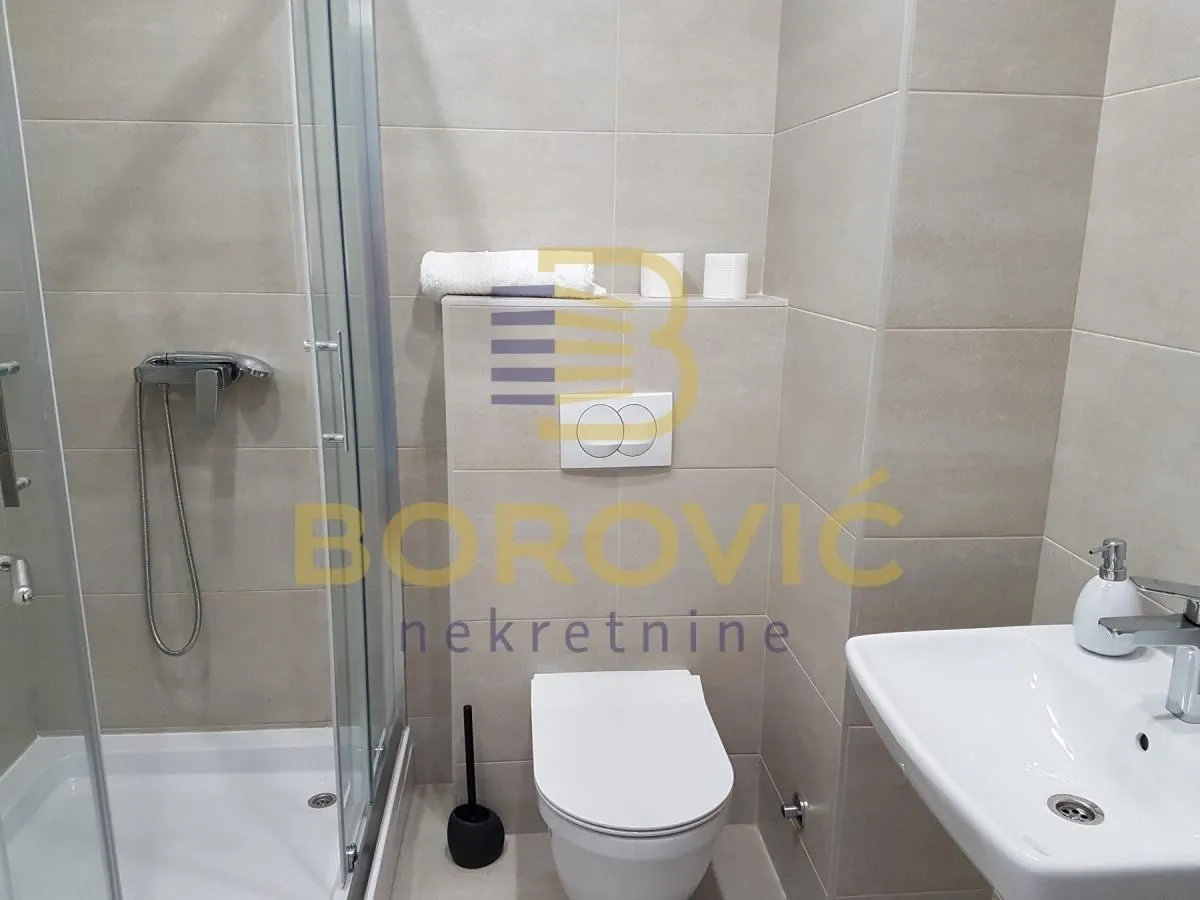 Modern bathroom with a shower cabin, washbasin, and toilet in beige tiles.
