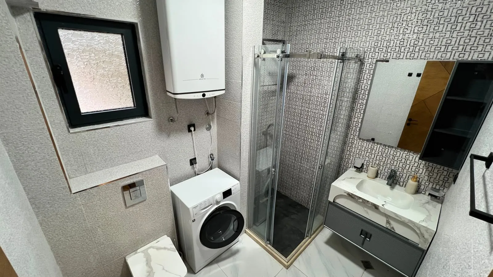 Modern bathroom with a shower cabin, washbasin, and washing machine.