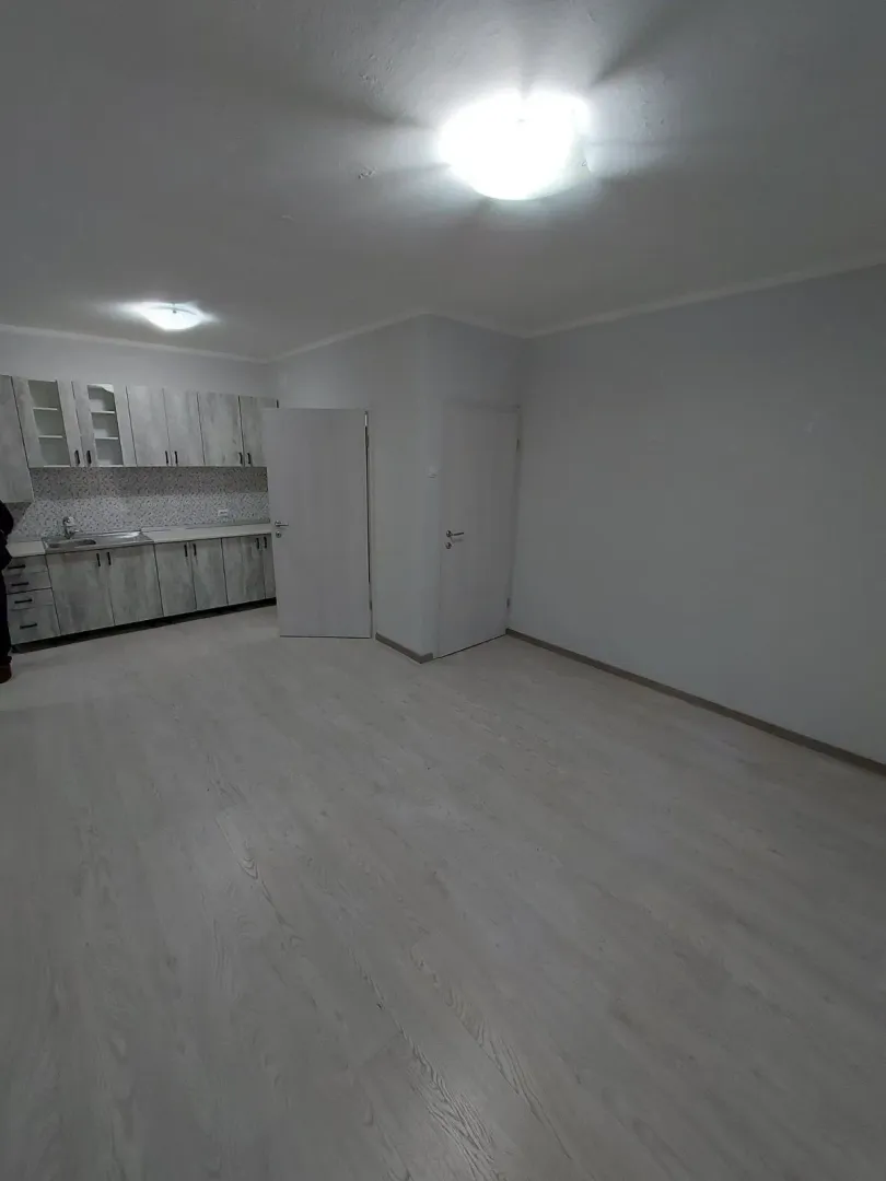 Prazna prostorija sa kuhinjskim elementima u pozadini.