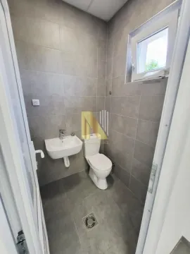 Smaller bathroom with grey wall and floor tiles, a washbasin and a toilet. - image 9