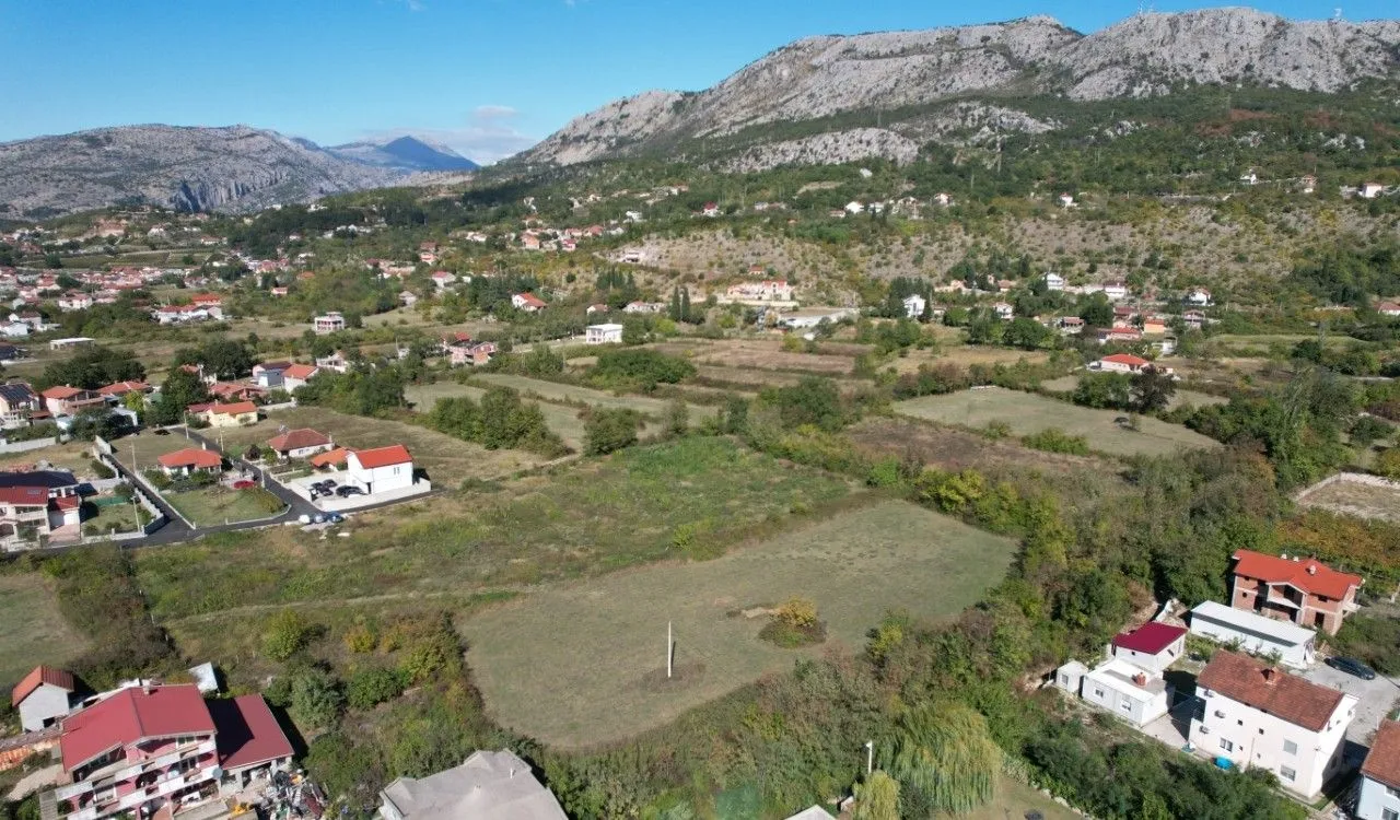 Pogled iz vazduha na zemljište i okolno naselje sa planinama u pozadini.