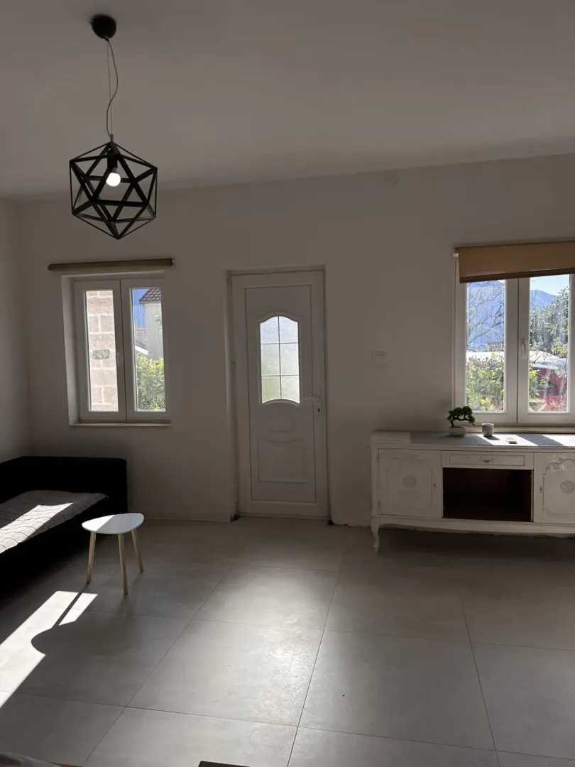Prostrana dnevna soba sa garniturom, komodom i modernim lusterom.