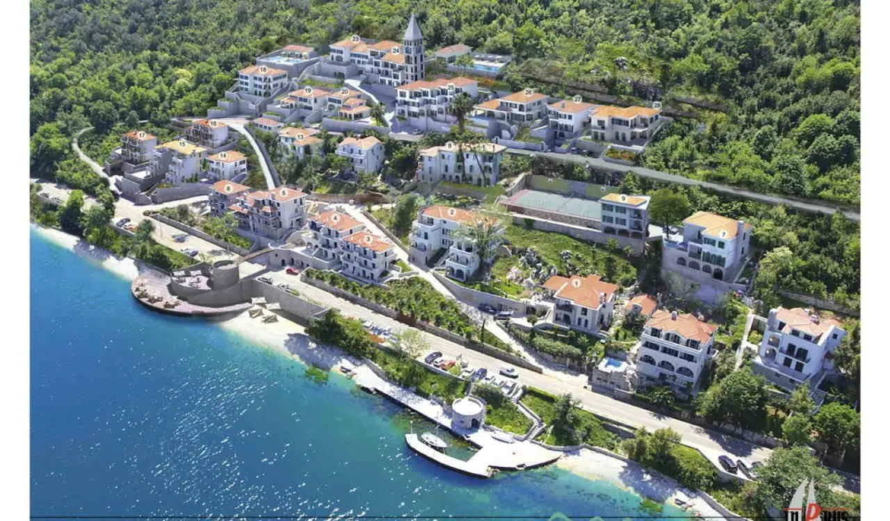 Pogled iz vazduha na kompleks zgrada pored obale mora sa uređenim zelenilom.