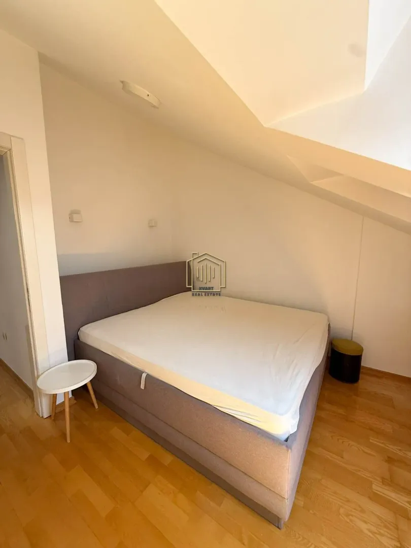 Bedroom with a double bed under a sloped ceiling and wooden flooring.