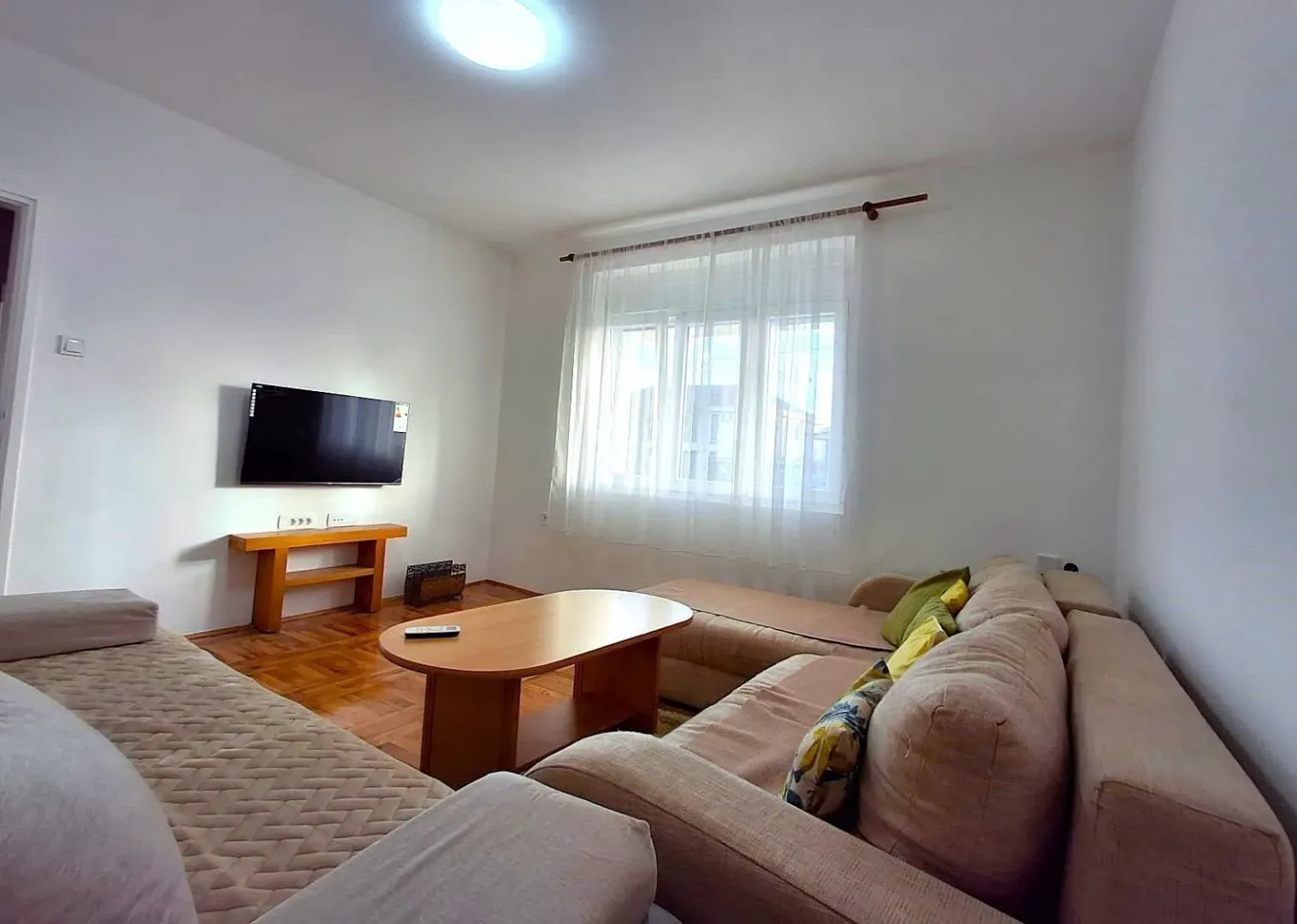 A bright living room with a seating set and a wall-mounted TV.