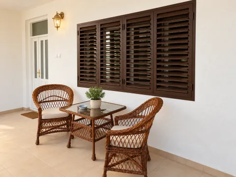 Covered terrace with wicker furniture and brown window shutters. - image 12