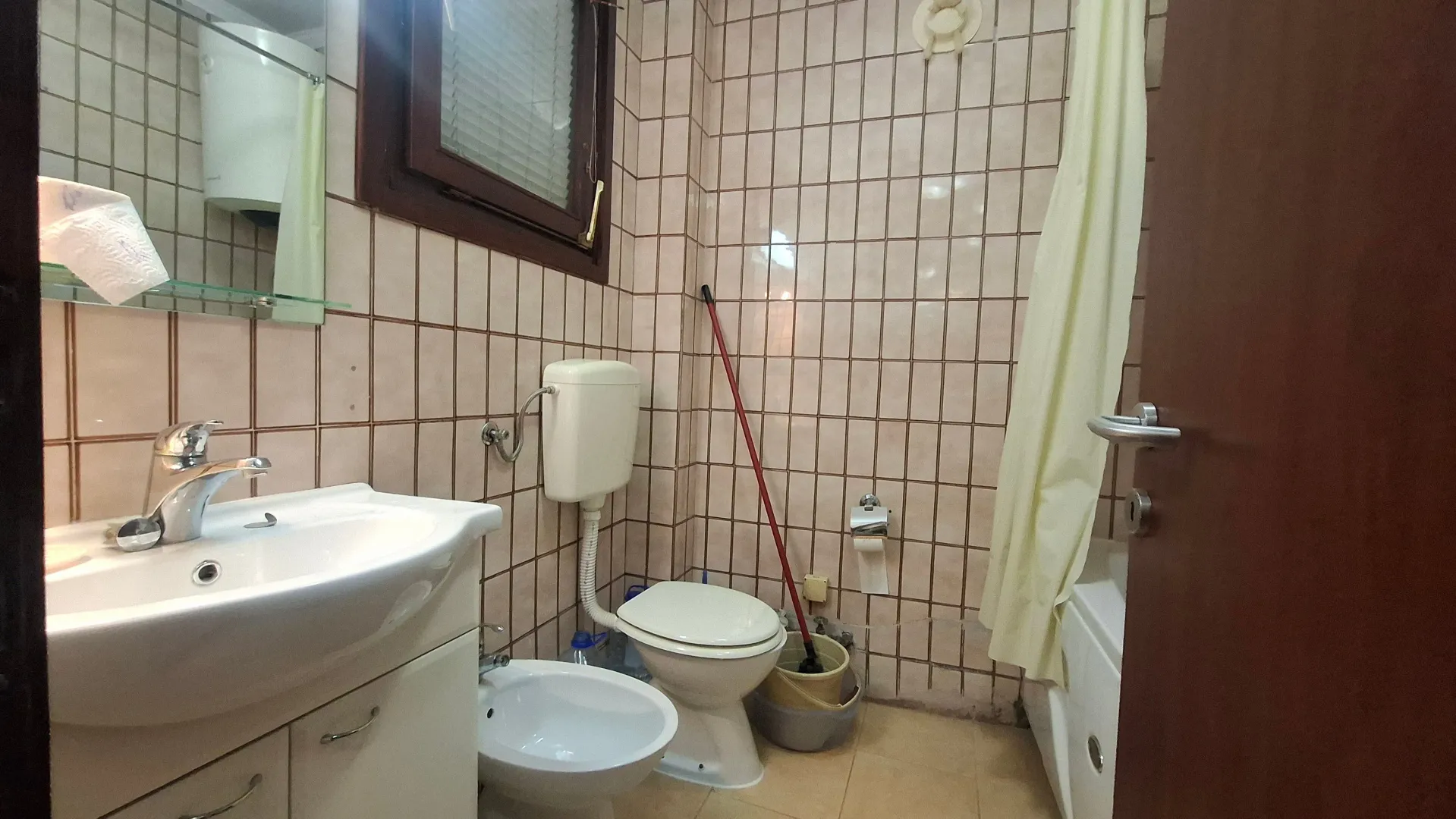 Manje kupatilo obloženo keramičkim pločicama sa umivaonikom, šoljom i kadom.