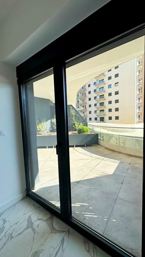 View through the balcony door onto a spacious terrace overlooking a building.