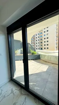 View through the balcony door onto a spacious terrace overlooking a building. - image 11