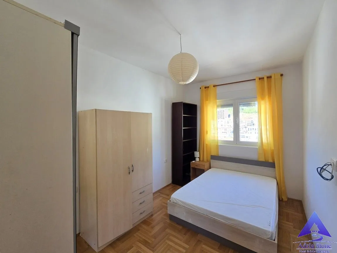 Namještena spavaća soba sa bračnim krevetom, ormarima i prozorom sa žutim zavjesama.
