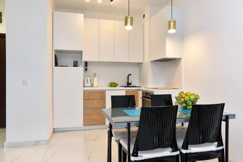 Modern white kitchen with wooden details and a dining table in the foreground. - image 3