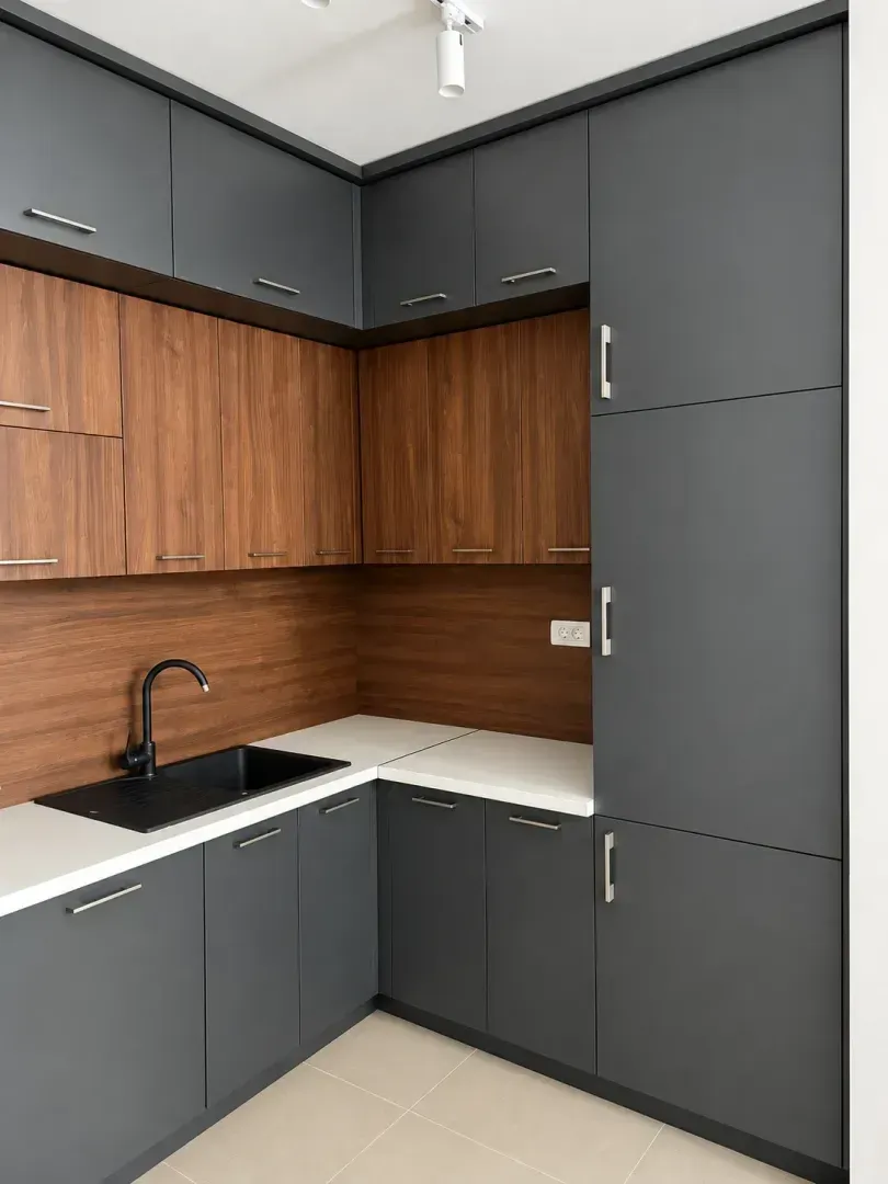 Moderna kuhinja sa tamnim elementima, drvenim detaljima i bijelom radnom pločom.