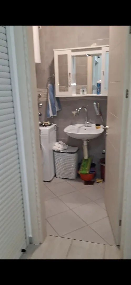 Pogled na kupatilo sa umivaonikom, ogledalom i veš mašinom.