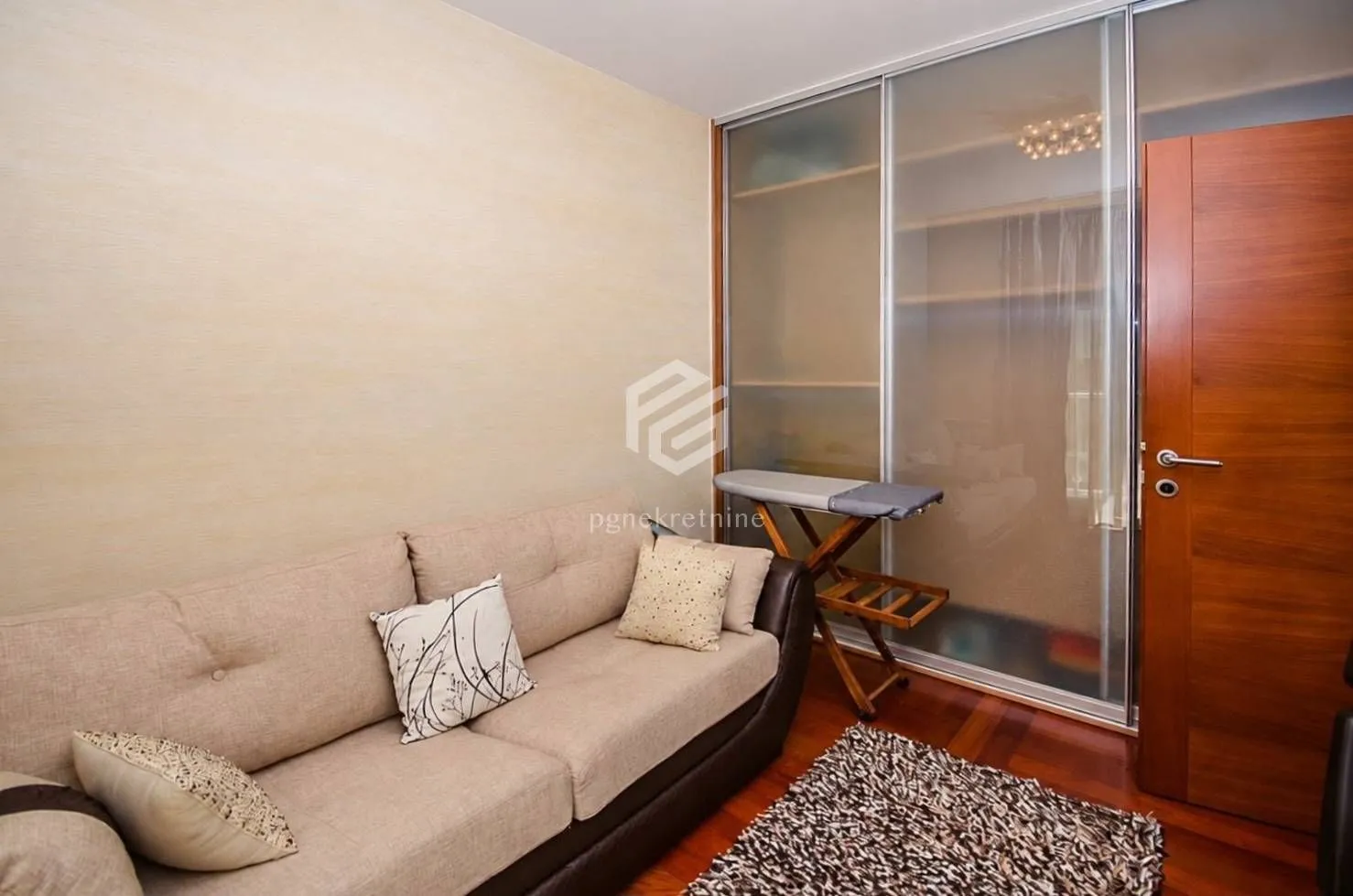 Living room with a beige sofa and a built-in wardrobe with sliding glass doors.
