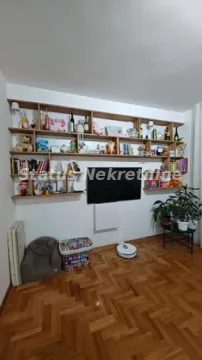 Dnevna soba sa drvenim parketom, TV-om na zidu i zidnim policama sa knjigama i dekoracijom. - image 8