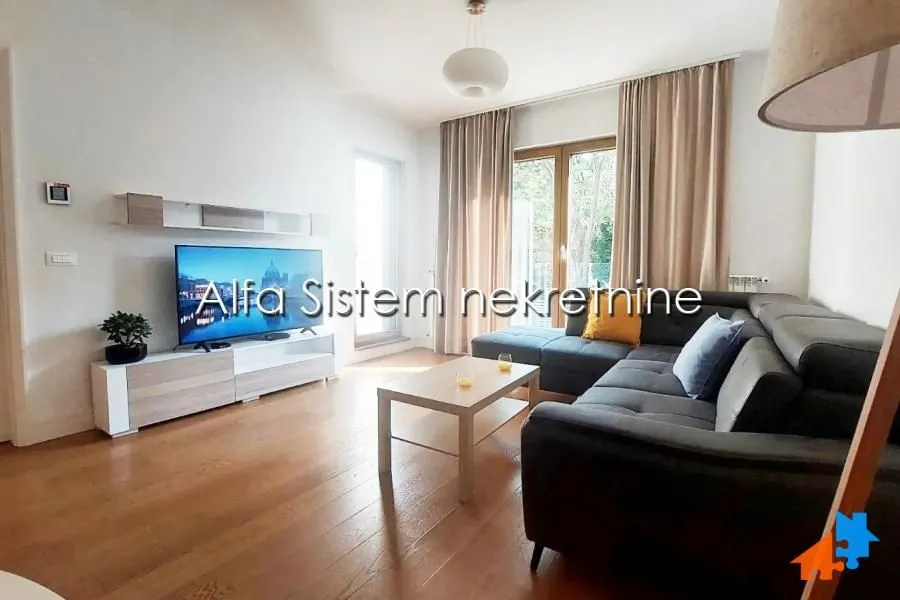 Dnevna soba sa ugaonom garniturom, televizorom i izlazom na terasu.