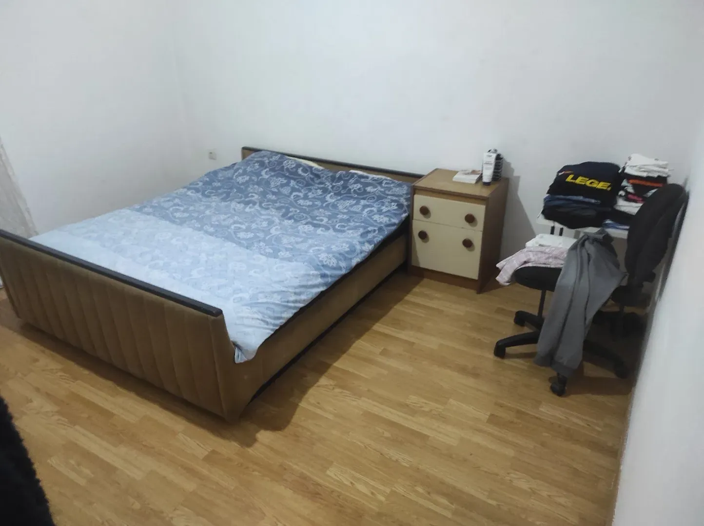 A simply furnished bedroom with a double bed and wooden flooring.