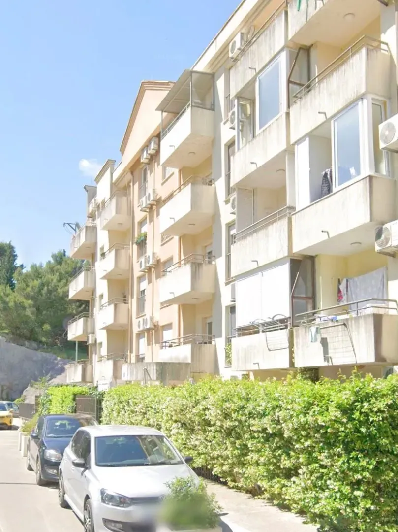 Spoljašnji izgled stambene zgrade sa balkonom i uređenim dvorištem.