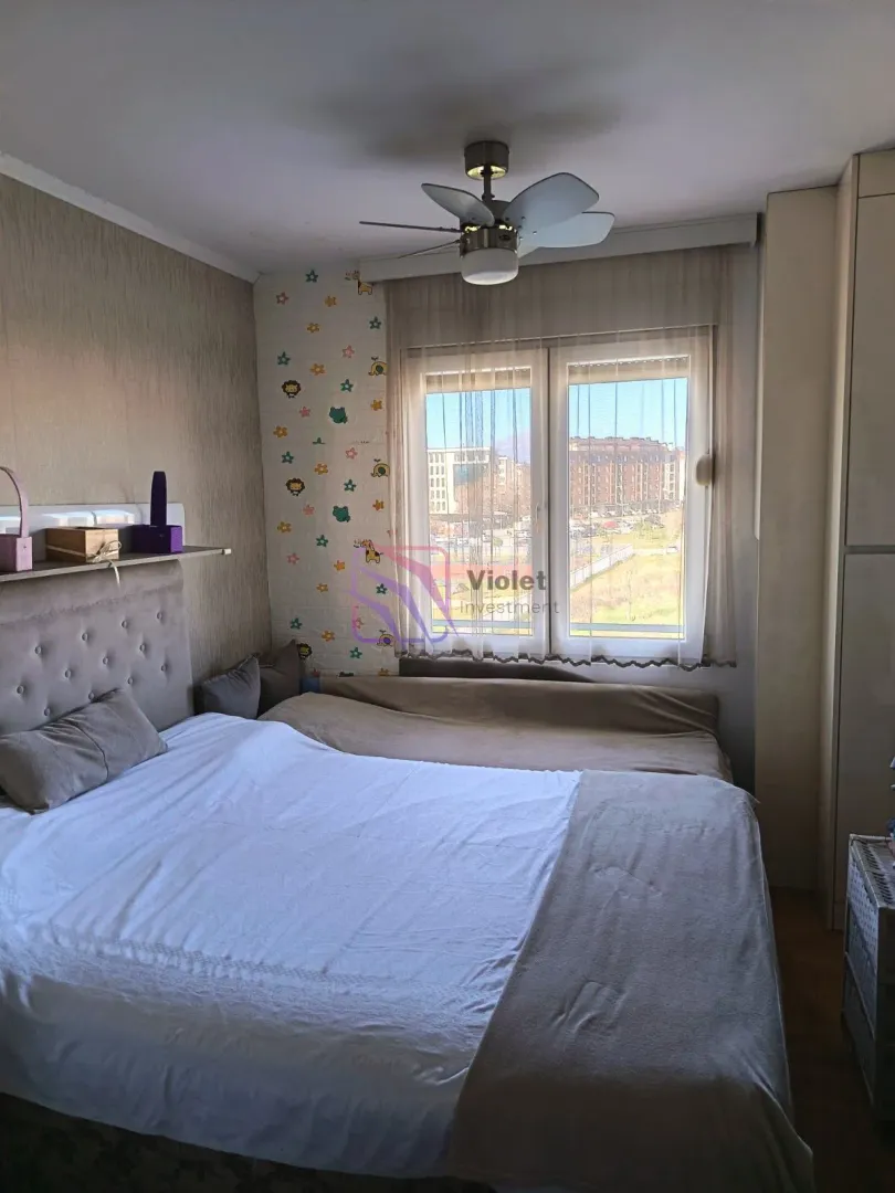 Spavaća soba sa velikim bračnim krevetom, prozorom i plafonskim ventilatorom.