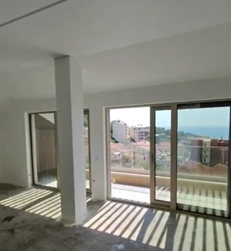 Prazna prostorija sa velikim prozorima i pogledom na grad i more.