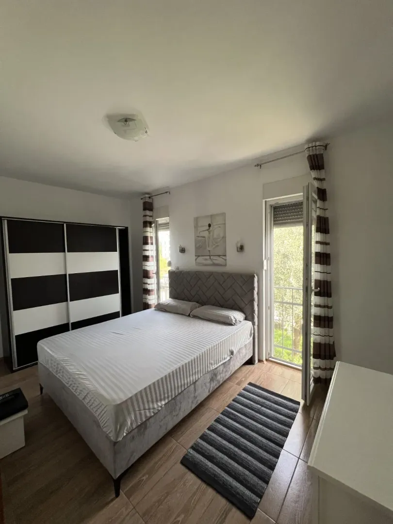 Svijetla spavaća soba sa bračnim krevetom, garderoberom i izlazom na balkon.