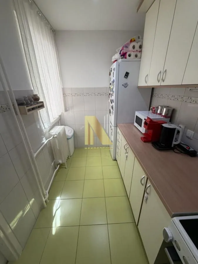 Manja kuhinja sa svetlim elementima, radnom površinom i frižiderom.