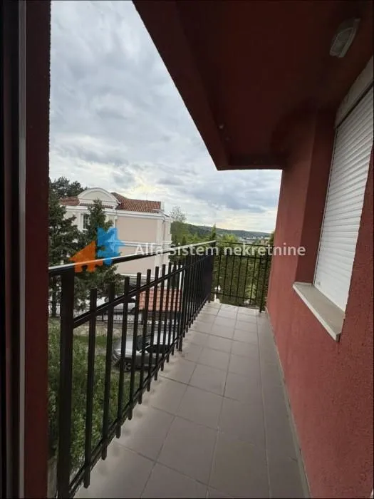 Natkriveni balkon sa metalnom ogradom i pogledom na okolinu.