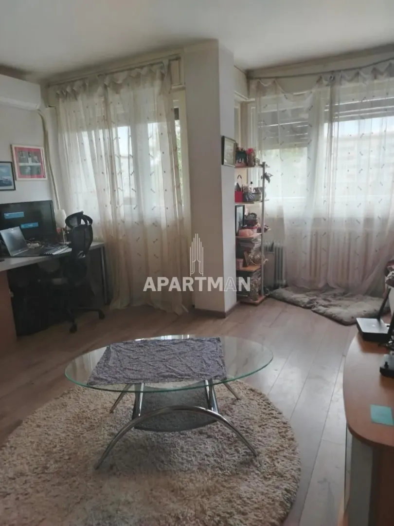 Living room with a seating area, a desk, and large windows.