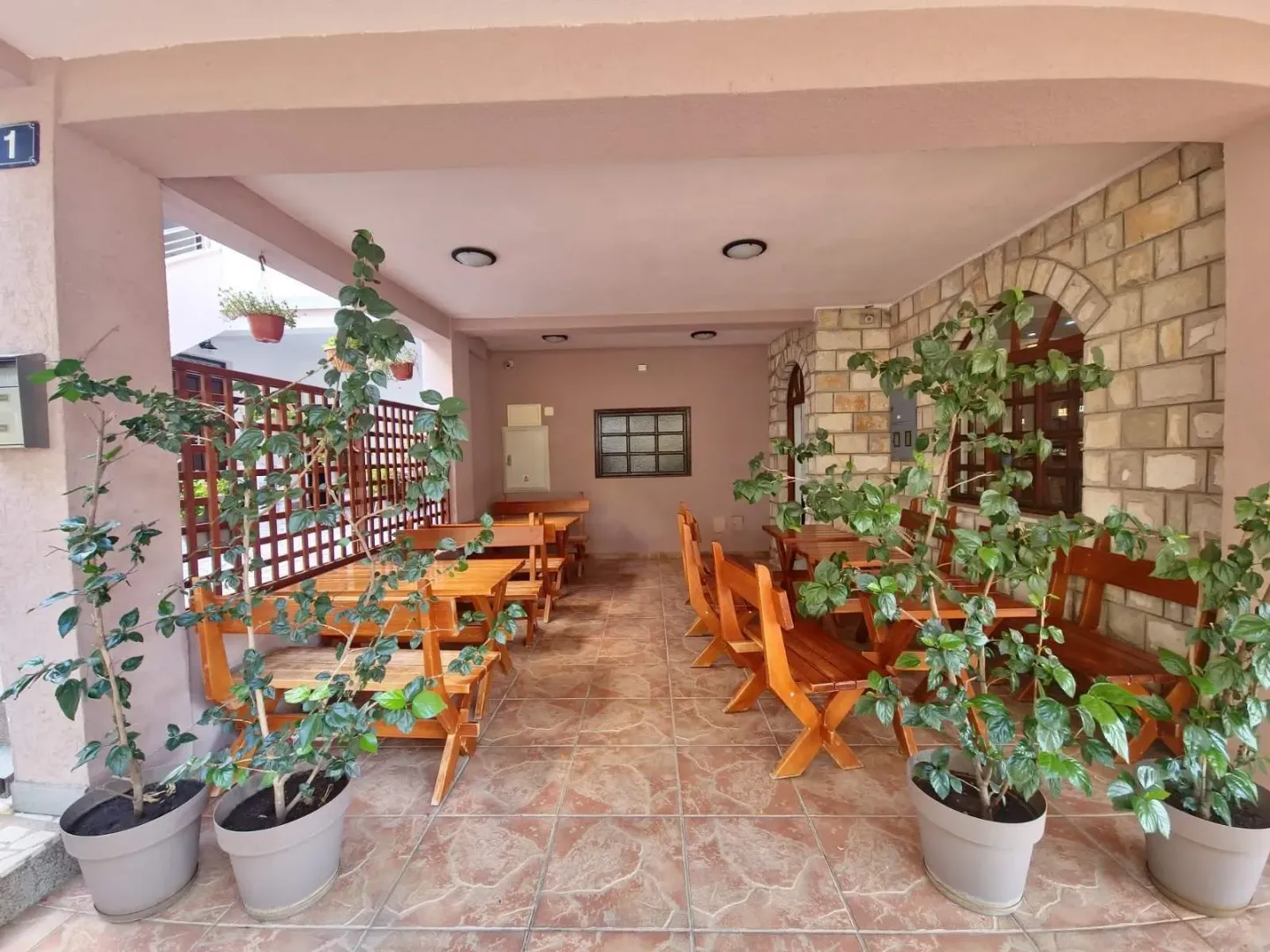 Covered terrace with wooden tables and benches, decorated with potted plants.